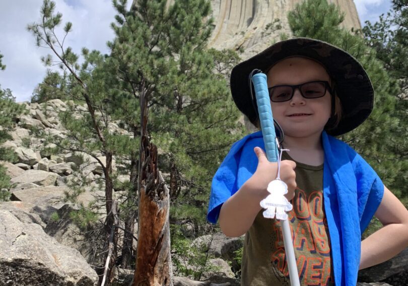 A young boy holding a pole in front of devils tower.