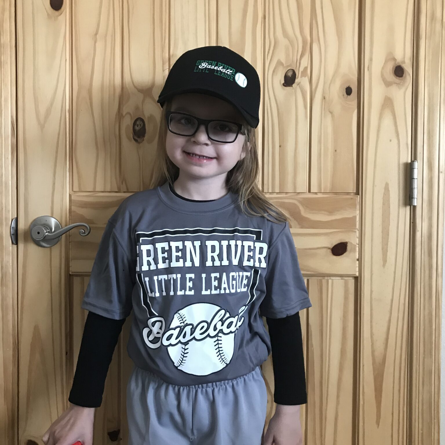 A little girl wearing a green river little league t - shirt.