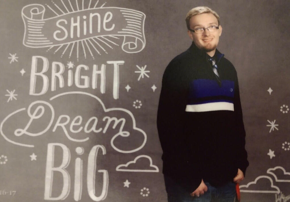 A man standing in front of a chalkboard that says shine bright dream big.