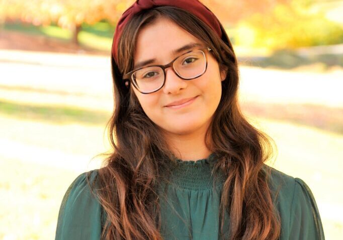 A young woman in glasses standing in front of a tree.