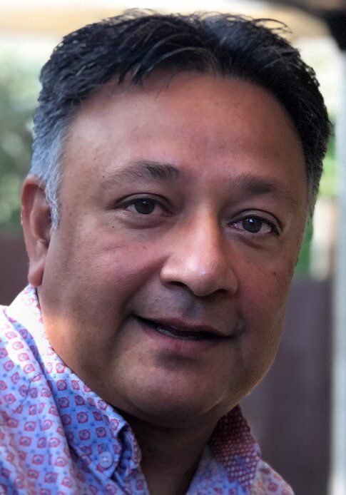 A man in a pink shirt is smiling at the camera.