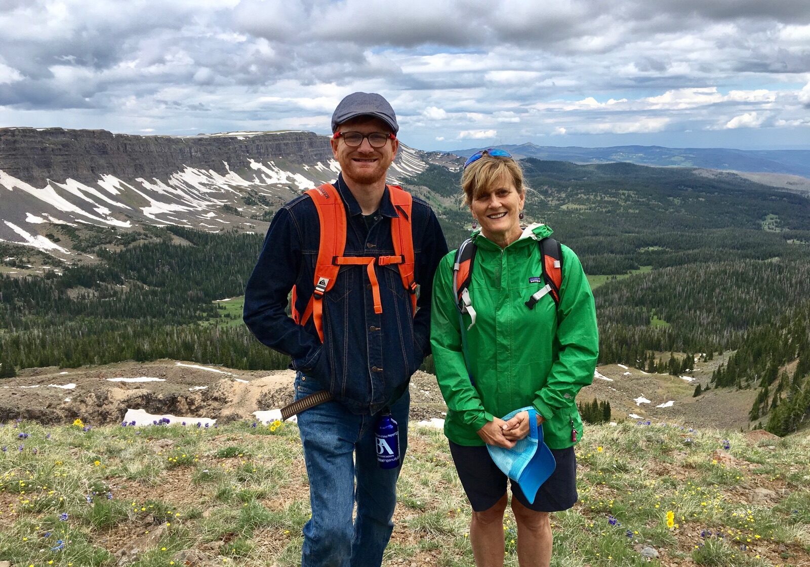 Two people standing on top of a mountain with mountains in the background.