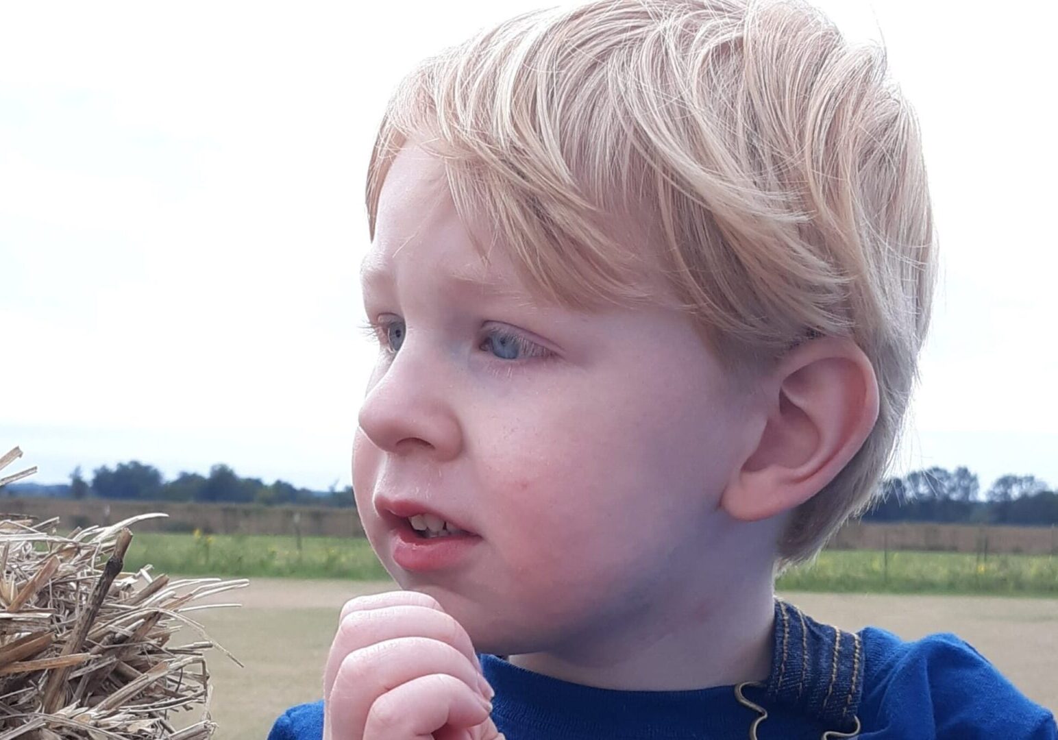 A young boy holding a straw bale.