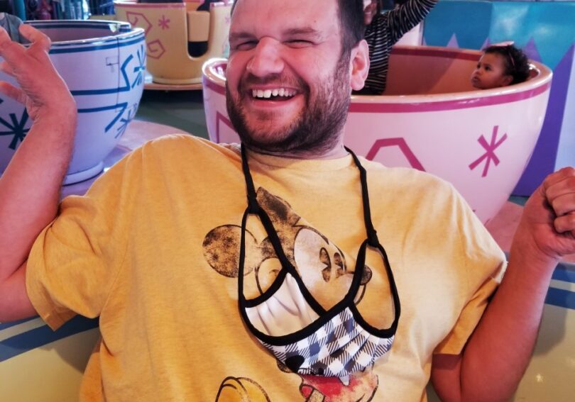 A man in a yellow t - shirt is posing for a picture at disneyland.