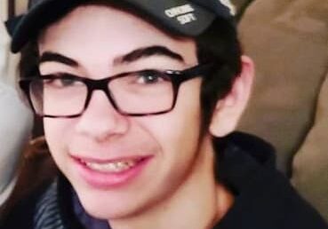 A young man wearing glasses and a hat is sitting on a couch.