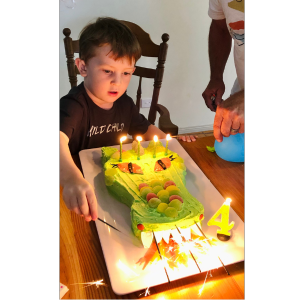 A boy blowing out candles on a green crocodile birthday cake.