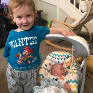 Two young boys standing next to each other in a baby swing.