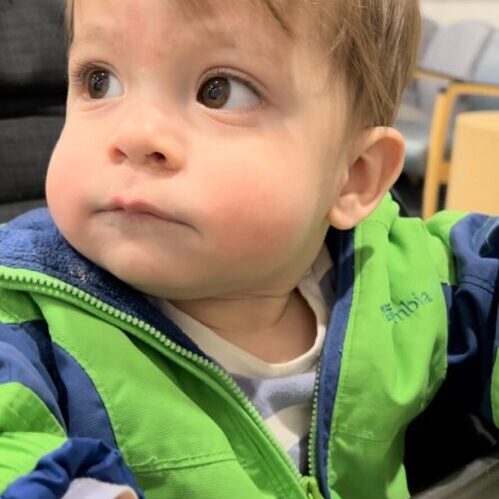 A young boy in a green jacket sitting in a car seat.