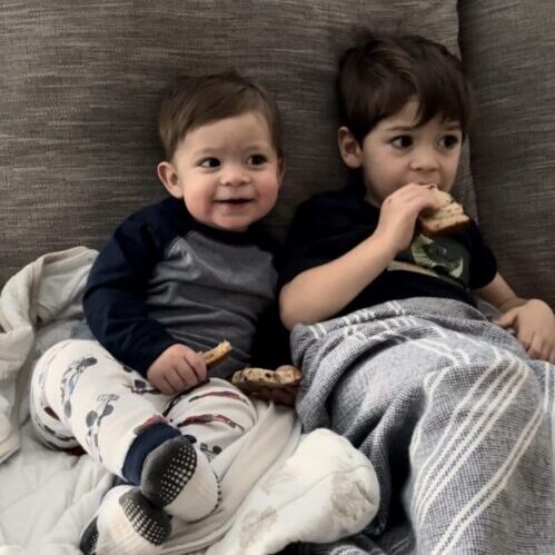 Two boys sitting on a couch with a blanket.