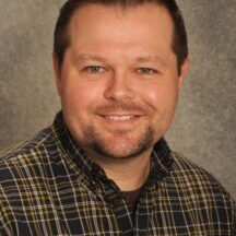 A man in a plaid shirt smiling for the camera.