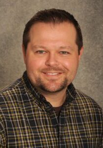 A man in a plaid shirt smiling for the camera.