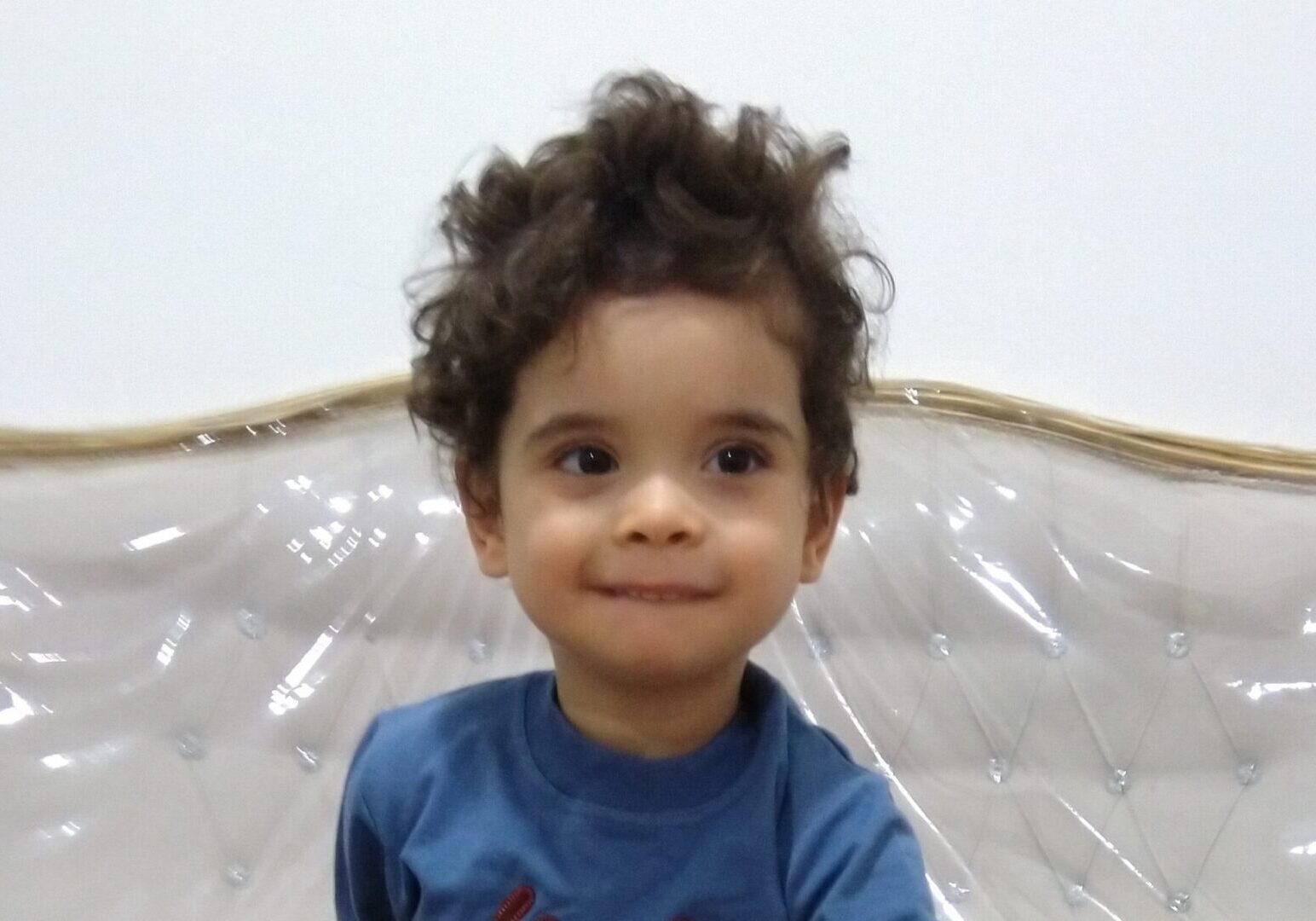 A young boy with curly hair sitting on a bed.