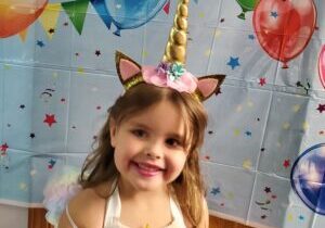 A little girl in a unicorn costume standing in front of balloons.