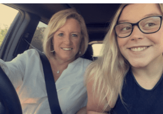 A mother and daughter smiling while driving in a car.