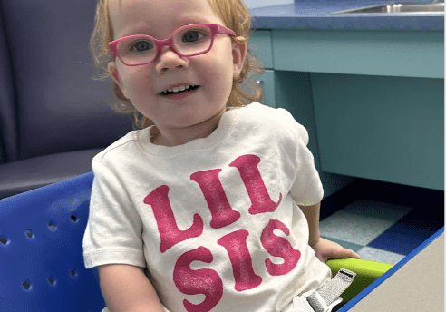 Young girl wearing glasses and "Lil Sis" shirt.