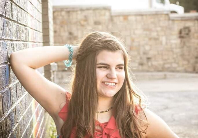 A young girl leaning against a brick wall.