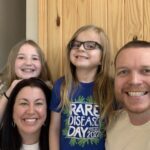 A family posing for a photo with a sign saying rare disease day.