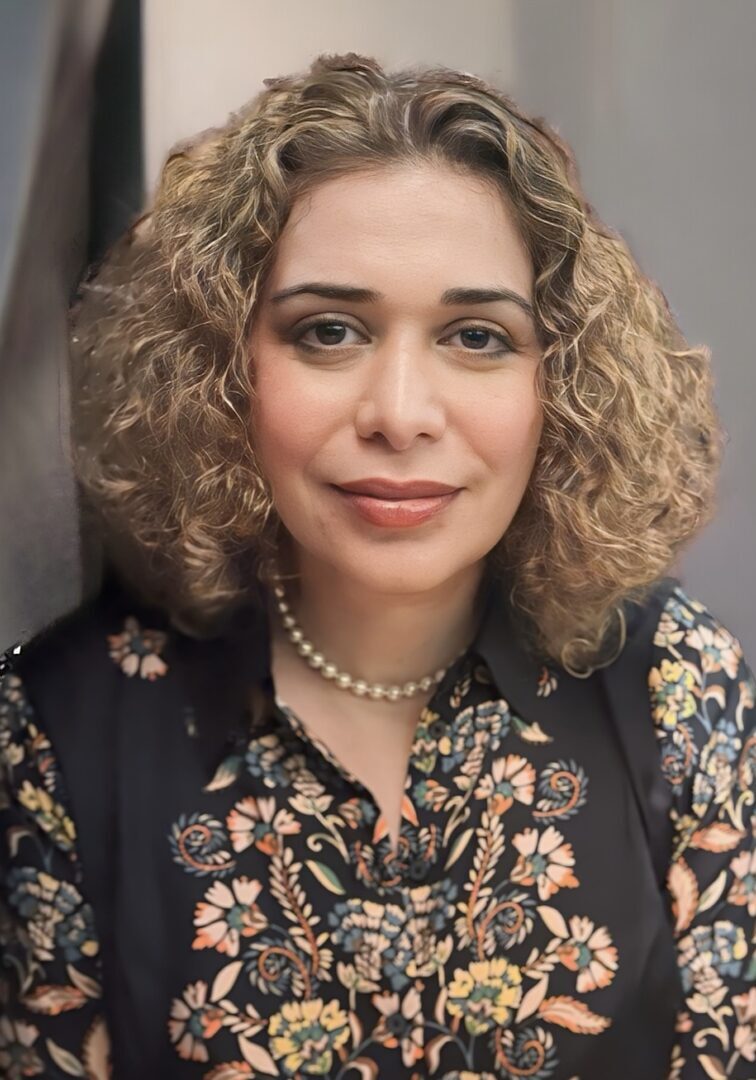 Headshot of a woman with curly hair and a floral shirt.