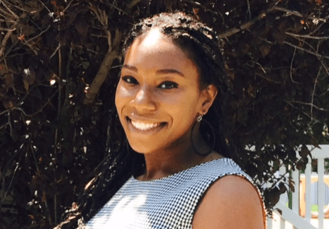 A black woman smiling in front of a tree.