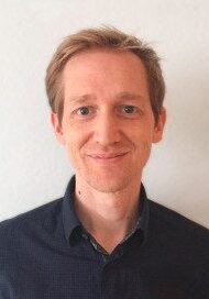 A man smiling in front of a white wall.