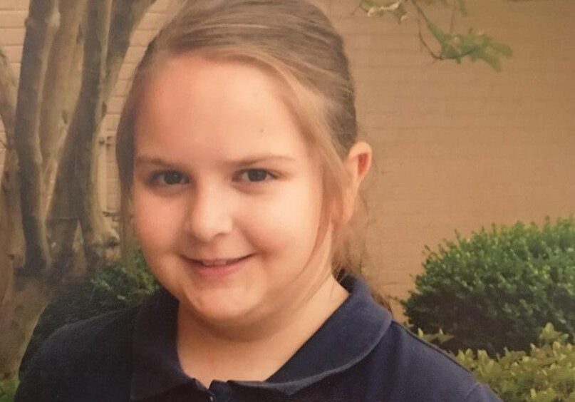 A young girl in a blue shirt smiles for the camera.