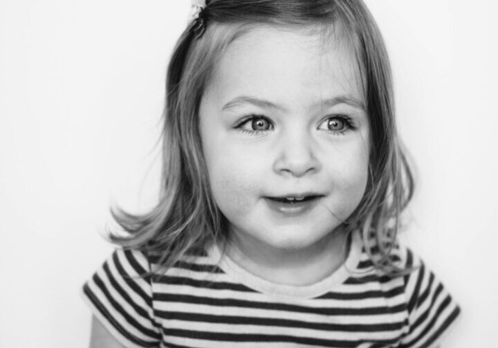 A black and white photo of a little girl in a striped dress.