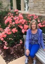 A woman sitting on a bench in front of roses.