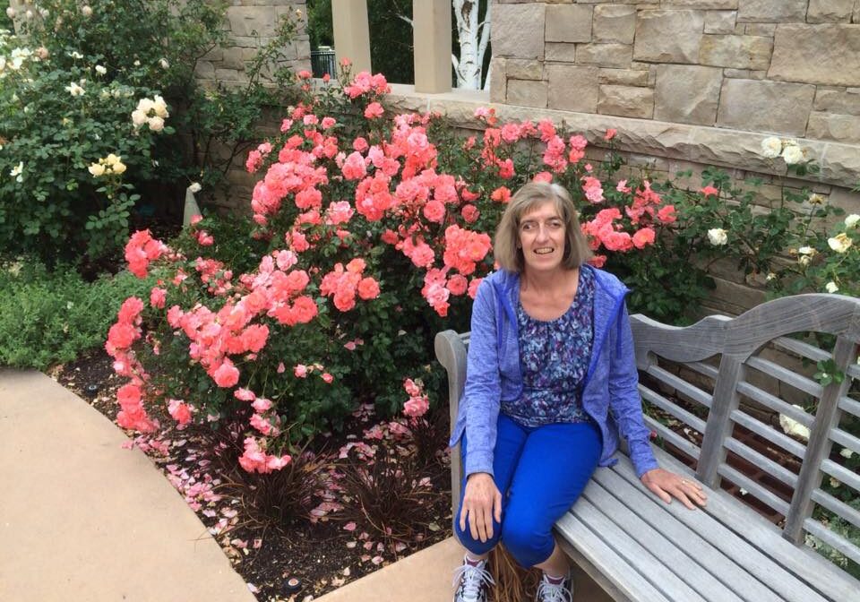 A woman sitting on a bench in front of roses.