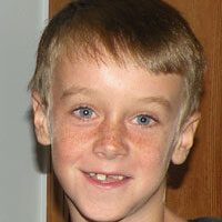 A young boy in a black shirt smiling for the camera.